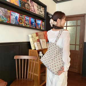 Gros plan du sac cabas en toile beige avec pois rouges et motif nœud porté par un mannequin