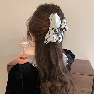 Detail of a large white satin bow hair claw with black trim and pearl center on model