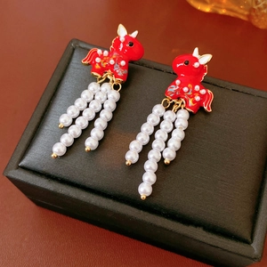Detail of red enamel horse earrings with white pearl tassels on a black display box