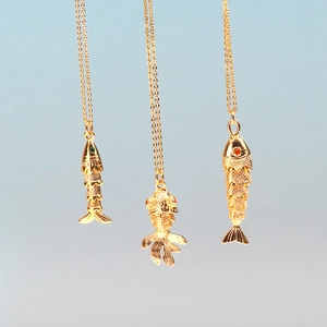 Detailed view of three vintage gold koi fish pendants with red and green gemstone eyes