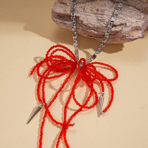 Detail view of a red crystal beaded bow and silver textured chain on a wooden base