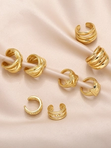 Close-up of gold layered ear cuffs and crisscross clip earrings on champagne satin fabric