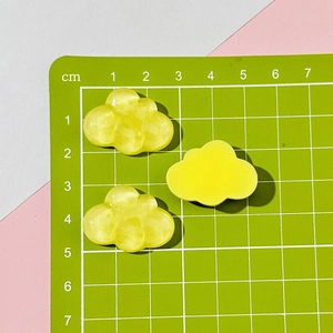 Macro view of three yellow resin cloud charms showing marble texture on a green mat