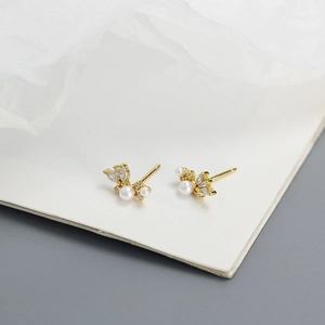 Macro shot of gold pearl earrings with zircon inlay in asymmetric floral design
