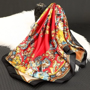 Detail of red floral satin scarf with paisley prints draped on a black chain bag