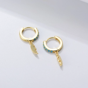 Macro detail of gold feather pendant earrings featuring small turquoise blue stone beads