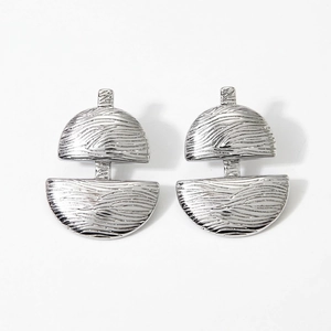 Détail macro de boucles d'oreilles géométriques argentées au motif de vagues abstrait