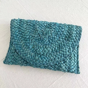 Detailed top view of a handmade lake blue woven straw envelope clutch bag on fabric