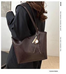 Detail view of large dark brown tote bag with baseball bat charm on a model's shoulder