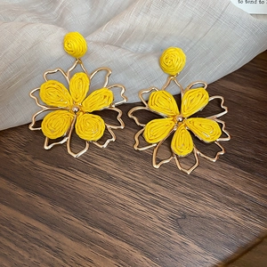 Close-up of yellow woven raffia flower earrings with golden hollow metal frames