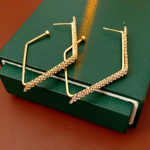 Dettaglio di orecchini geometrici dorati con diamanti su una scatola per gioielli verde