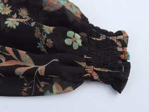 Nahaufnahme der gesmokten Manschetten an einem schwarzen Chiffonkleid mit Blumenmuster