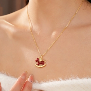 Close-up of a golden rocking horse necklace with red enamel and zircon details on model