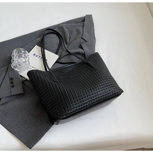 Close-up of black woven leather tote bag texture on a grey suit with lifestyle props