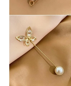 Detailed view of a golden butterfly brooch with clear crystals and a large pearl accent