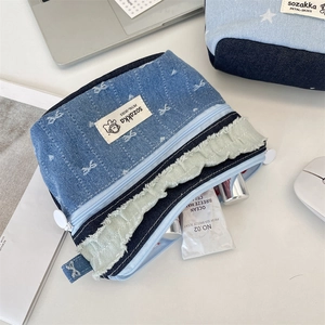 Detail of denim patchwork makeup bag showing raw edges and brand label on desk