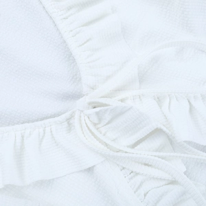 Détail du haut en tissu gaufré blanc avec bords à volants et fines lanières à nouer
