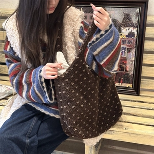 Detail of a brown faux shearling tote bag with polka dots held by a model on a bench