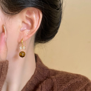 Close-up of golden bow earrings with tiger eye stone pendant worn by a model