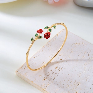 Detailed macro view of golden alloy bangle featuring red rose enamel and green leaf accents