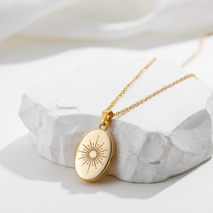 Golden oval locket necklace with sunburst engraving on a minimalist stone display