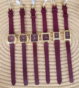 Collection of women's gold watches with purple leather straps on a woven mat background