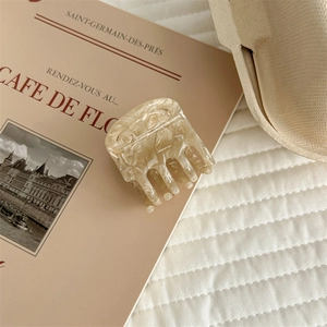 Detail view of a beige marble acetate hair claw clip on a French vintage style book background