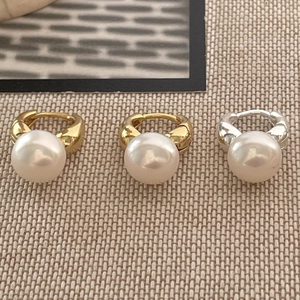 Close-up of minimalist round white pearls with gold and silver studs on beige texture