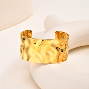 Detail of wide gold-colored stainless steel cuff bracelet with irregular wave texture