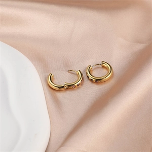 Close-up of gold-plated hoop earrings featuring purple and pink zircon on beige satin