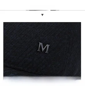 Close-up of navy blue twill fabric and matte metal M logo detail on a winter baseball cap