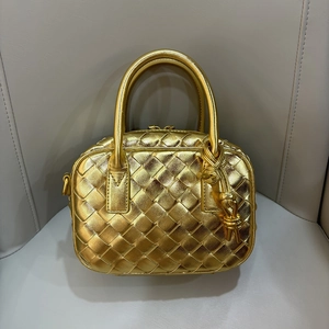 Close-up of golden woven leather mini pillow bag with top handle and side knot detail