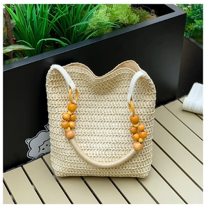 Detail view of woven straw bucket bag with unique wooden bead handle on a wooden bench