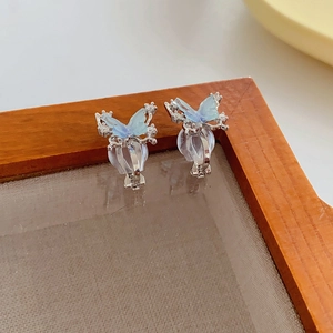 Close-up of 18k gold plated zircon butterfly ear clips in light blue on a wooden tray