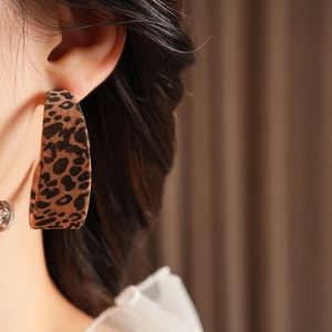 Close-up of leopard print velvet C-shaped hoop earrings worn by a model in soft light