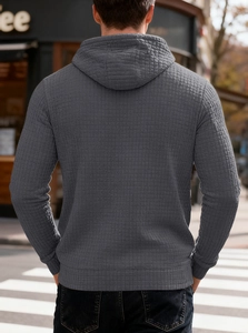 Rear view of men's dark grey hoodie showing waffle texture and ribbed cuffs in urban setting