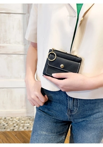 Detail of a black leather key pouch with white stitching and gold zipper held by a hand