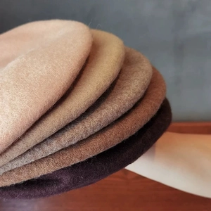 Detailed close-up showing stacked wool berets in beige, camel, and khaki earth tones