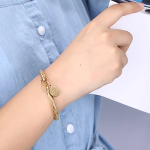 Detail of a gold cable texture bangle featuring a St. Benedict religious pendant and clasp