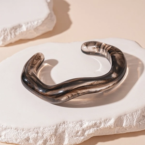 Macro detail of wave-shaped acrylic cuff with dark grey marble texture and glossy finish
