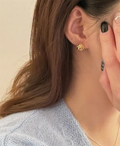Primer plano de elegantes pendientes de nudo dorado usados con un tejido azul claro