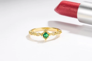 Macro view of gold-tone ring featuring a round emerald center stone and white side diamonds