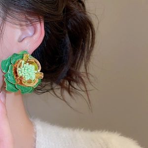 Gros plan d'une boucle d'oreille fleur verte avec bord doré sur un look vintage chic