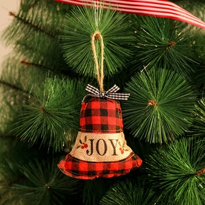 Gros plan d'une cloche en tissu à carreaux rouge avec JOY suspendue au sapin de Noël