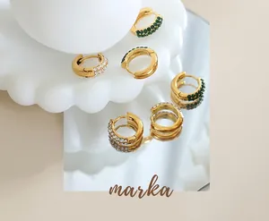 Macro detail of 18K gold plated hoop earrings with emerald and clear zircon stones