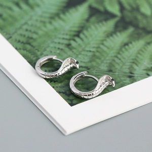 Detailed macro shot of silver cobra hoop earrings with black stone eyes and textured scales