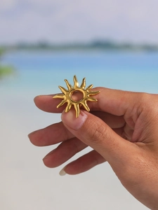 Detailed close-up of a golden sunburst ring on hand with a coastal background