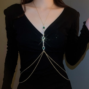 Detailed close-up of golden body chain featuring green crystals and sparkling tassel fringe