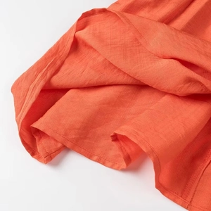 Gros plan détaillé montrant la texture du tissu orange et le tissage premium du pantalon