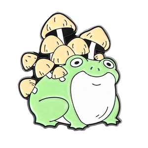 Detail showing a green cartoon frog enamel pin with small yellow mushrooms on its back